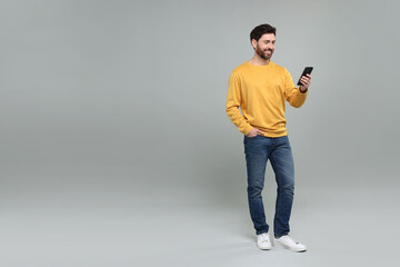 Smiling man with smartphone on grey background. Space for text