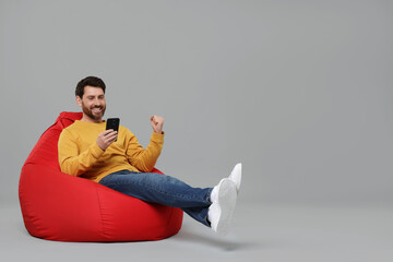 Happy man with smartphone sitting on bean bag against grey background. Space for text