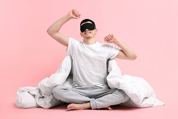 Happy man in pyjama with sleep mask and blanket on pink background