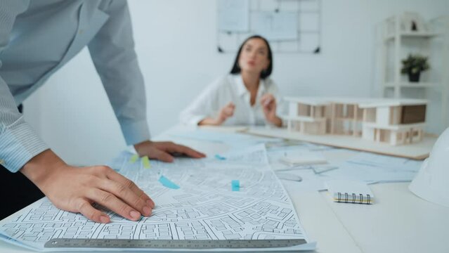 Skilled caucasian interior designer working with house model while discussing with asian architect engineer about house plan on meeting table with blueprint and house model scatter around. Immaculate.