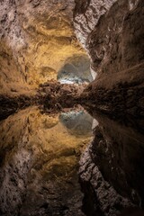 Vertical shot of a hidden cave with still water reflecting the cave walls