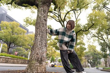 公園の木に触れて遊ぶ若い女性