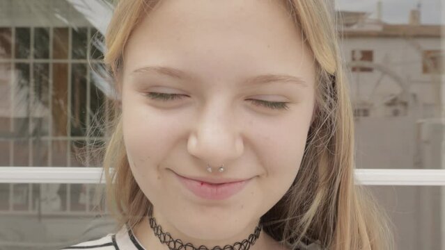 portrait of smiling Generation Z teenage girl with  nose piercing and choker around her neck, turning towards  camera and sticking out her tongue