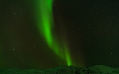 Beautiful shot of bright green aurora northern lights over mountains in Norway