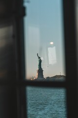 Vertical shot of the statue of liberty behind a boat window