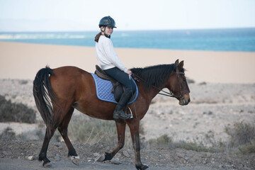 Beautiful young girl riding her horse in the desert and dunes of Fuerteventura