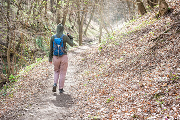 Young woman tourist with backpack and walking stick hiking the forest path