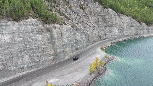 Aerial view of a car driving on a highway road between the rocks and the sea