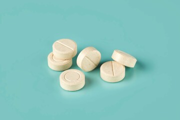 Closeup shot of six white tablets with a center line on a cyan background