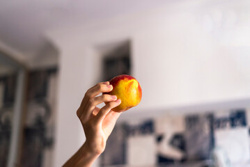 Closeup shot of a hand holding a red apple in the blurred background