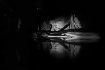 Grayscale closeup of a man in the darkness leaning on the glass surface with reflection.