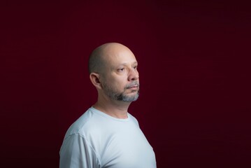 Fototapeta premium Portrait of a bald bearded man looking up against a red background