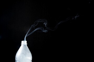 Smoke coming out of a plastic bottle on black background -  aromatherapy concept