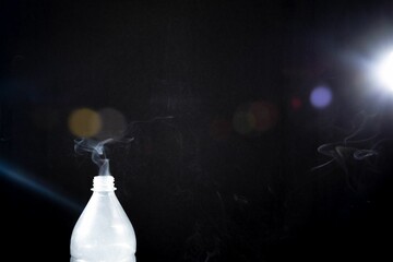 Smoke coming out of a plastic bottle on black background -  aromatherapy concept