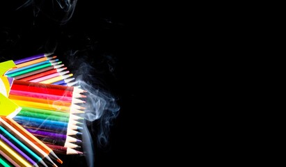 Closeup of colorful pencils and white smoke on a black background