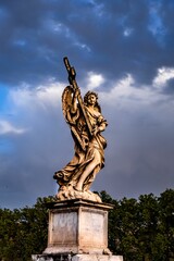 Marble angel statue holding the cross on the St. Angelo Bridge under cloudy sky in Rome, Italy