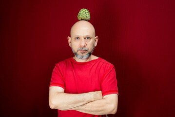 Funny man with a sugar apple on his head standing over a red background
