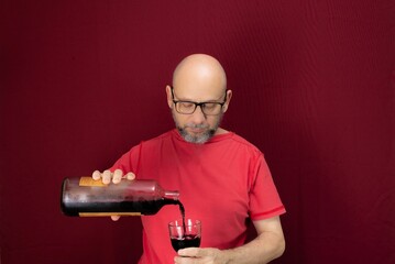Man pouring wine into a glass while standing over a red background