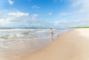 An adult woman in a bikini walking under strong sunlight on beac