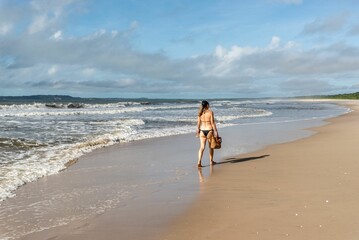An adult woman in a bikini walking under strong sunlight on beac
