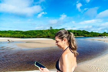 Woman looking at cellphone against forest river and sky in backg