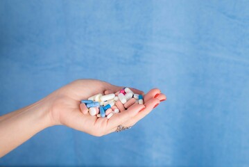 Pills in a persons palm against blue background. Medical supplies.