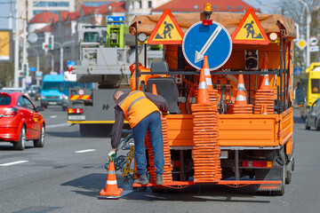 Worker in orange uniform on line striping truck places traffic cones on wet paint line until it dries. Road marking machine, wet paint spray, roadworks. Pant liner truck paint lines on city road