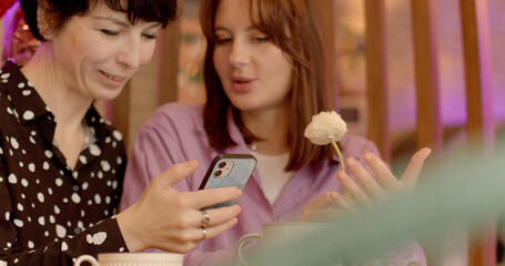 People with smartphone. Two women in a cafe. They are conversing, expressing emotions on their...