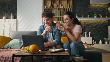 Pair laughing watching movie at home using laptop. Family weekend on cozy couch