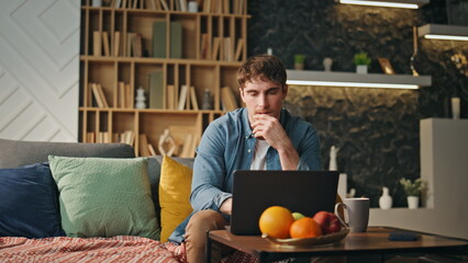 Tired worker focused laptop solving problem at home couch. Freelancer working 