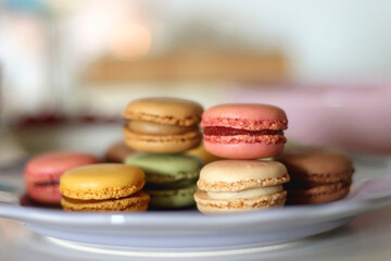 Plate of pastel macarons, cookies and chocolate, cup of tea of coffee, glass of bubble water, various berries, books and accessories on the table. Selective focus, pastel colors.