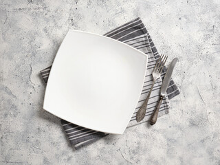 A large white empty plate, vintage fork and knife lie on a decorative towel on an abstract background.