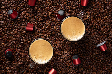 Top view of many roasted coffee beans and two glass cups with fresh espresso coffee. Capsules for coffee machines.