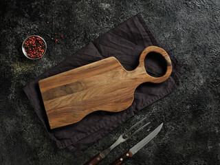 Top view of a beautiful wooden board, decorative fabric towel, fork, knife and spices.