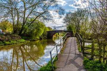 Fototapeta premium A view down the canal path towards a footbridge over the Grand Union Canal in Aylestone Meadows, Leicester, UK in Springtime