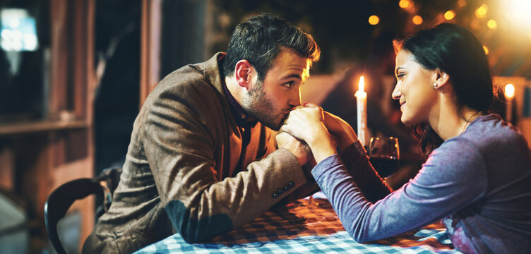 Romance, man and woman on date, night and kiss on hands with eye contact for anniversary together. Restaurant, fine dining and dinner for couple, love and female person in relationship with partner - Powered by Adobe