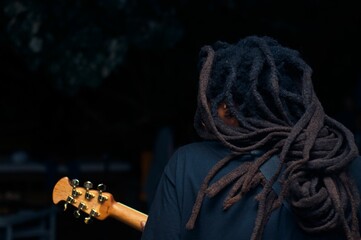 Musician with dreadlocks playing the guitar on a dark background