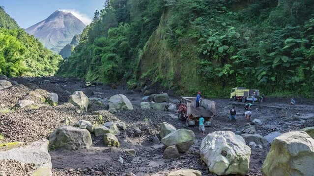 Yogyakarta, Indonesia - February 11, 2024. Morning activity of sand mining in the Boyong River with Merapi Mount in the background. Miners load the sand into trucks, then it is delivered to the buyer.