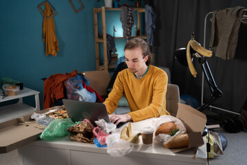 Young hipster male student working or studying in messy room in his home