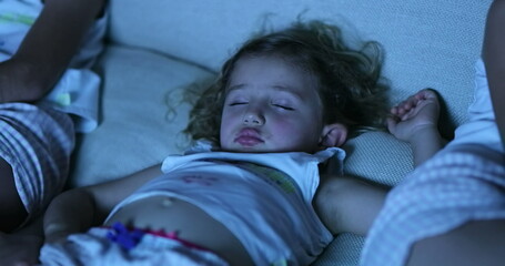 Little girl asleep in sofa in front of TV screen, real life child sleeping in front of movie