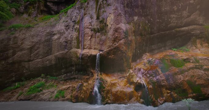 Chegem waterfalls. An amazing stream of water flows like a waterfall from a stone wall directly into a stormy river. Russia. Caucasus. Kabardino-Balkarian Republic.