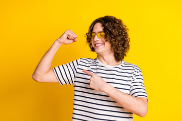 Photo portrait of nice teenager man point biceps look muscle dressed stylish striped clothes isolated on yellow color background