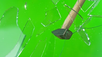 Freeze motion of glass-breaking hammer, shattering against green background