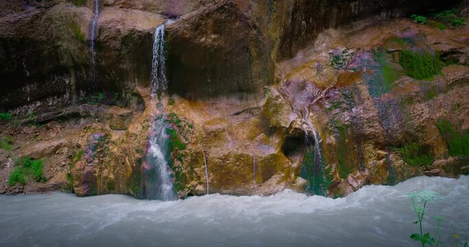 Chegem waterfalls. An amazing stream of water flows like a waterfall from a stone wall directly into a stormy river. Russia. Caucasus. Kabardino-Balkarian Republic.