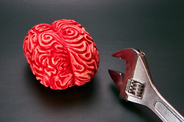 Red fake brain with a large wrench on a dark green background.