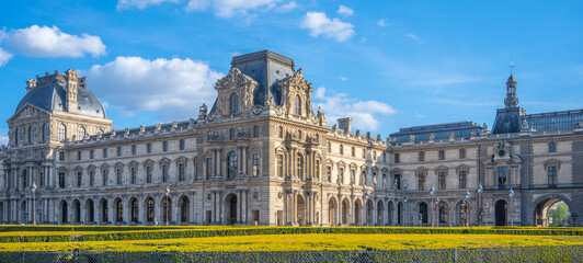 The majestic Louvre Museum basks in the sunlight against a clear blue sky, surrounded by manicured lawns. Paris, France