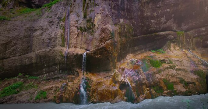Chegem waterfalls. An amazing stream of water flows like a waterfall from a stone wall directly into a stormy river. Russia. Caucasus. Kabardino-Balkarian Republic.