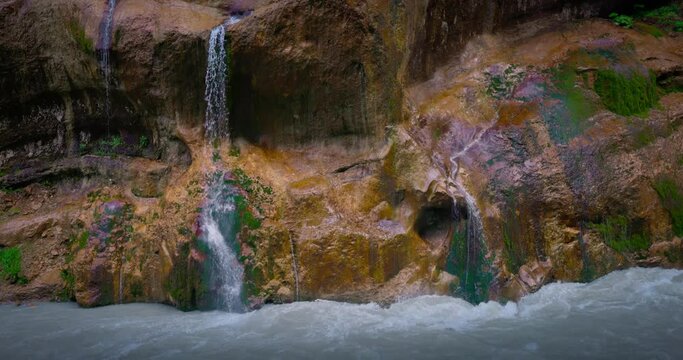 Chegem waterfalls. An amazing stream of water flows like a waterfall from a stone wall directly into a stormy river. Russia. Caucasus. Kabardino-Balkarian Republic.