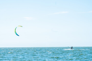 A kitesurfer harnesses the wind power, gliding across the sea's surface under a vast, clear sky....
