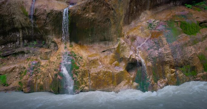 Chegem waterfalls. An amazing stream of water flows like a waterfall from a stone wall directly into a stormy river. Russia. Caucasus. Kabardino-Balkarian Republic.